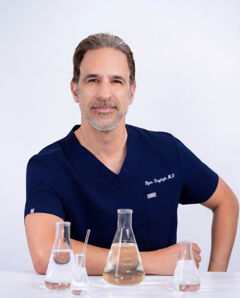 Dr. Bijan Haghighi, MD, in navy scrubs at a clean white surface with chemistry beakers.